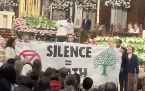 Protesters unfurl banner reading Silence = Death before altar. 