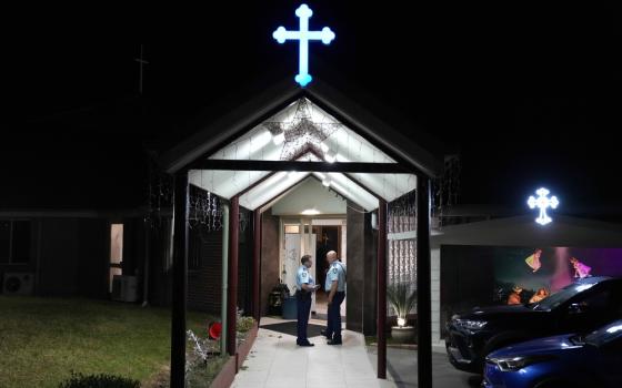 Two law enforcement officer stand beneath church portico at night, illuminated blue cross tops portico.