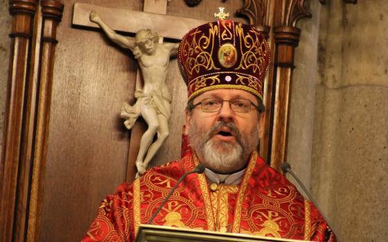 Bishop, vested in eastern style, delivers homily from lectern, crucifix in background. 