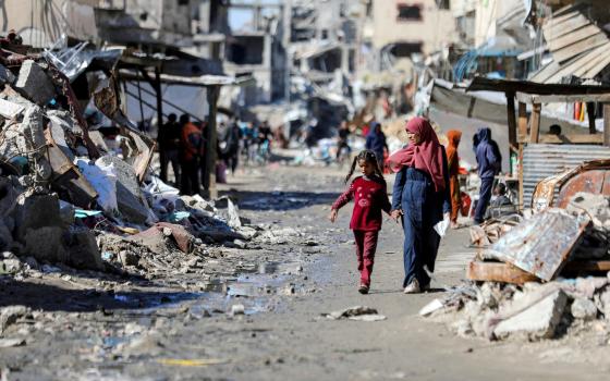 Women and young girl walk hand in hand through ruins. 