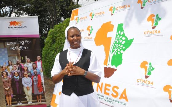 Sister stands with hands folded in front of organization banner