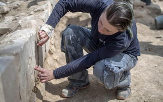 Archaeologist kneels down to examine stone structure