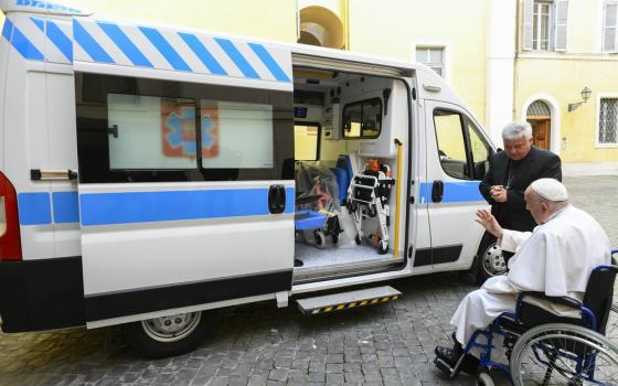 Pope Francis, in wheel chair, raises hand in blessing over ambulance