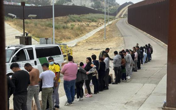 People line along border wall, facing official vehicle