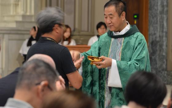 Pei, vested in green, hands Eucharistic host to person. 