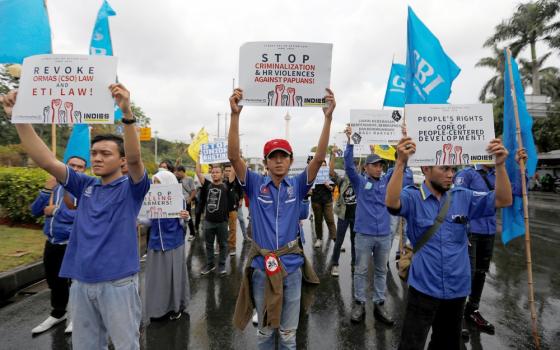 People wearing matching shirt and holding signs march through street. 