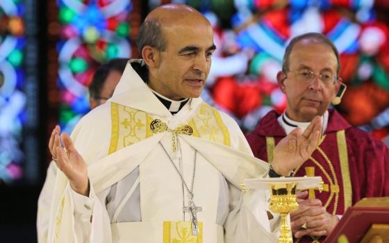 Zaidan, vested for Mass, raises hands in prayer at altar. 