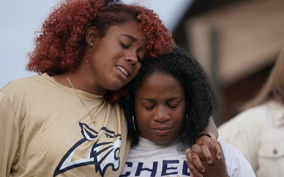 Two women stand side by side, one has her arm around the other. 