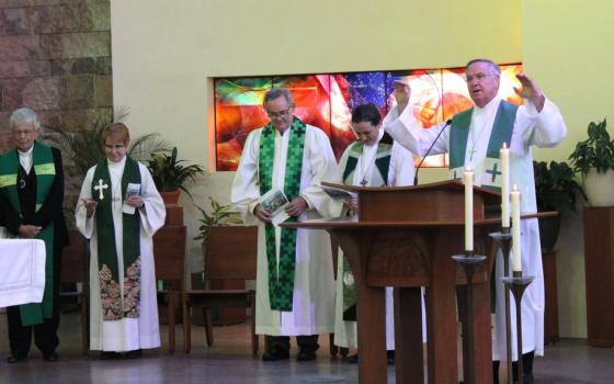 Dolan, vested only in choir robe and stole, stands at lectern with arms raised in blessing.