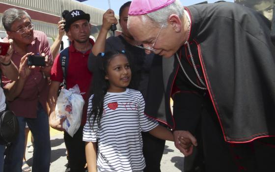 Seitz in purple-piped cassock and purple zucchetto, bends down to take little girl's hand. 