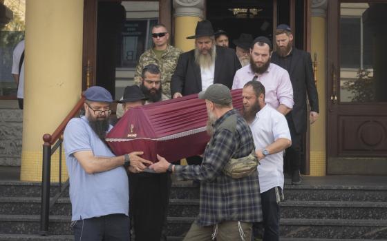 Azman follows pallbearers who gingerly carry coffin down exterior steps of synagogue.