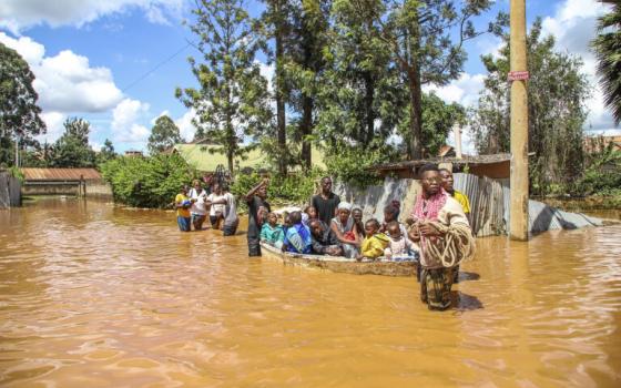 People on boat, and others wading through flooded street. 