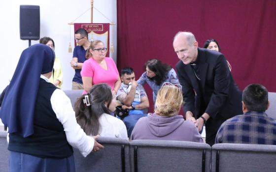 People sit and stand, some crying. The bishop bends down to shake a hand.