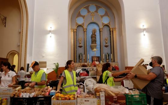 Volunteers wearing yellow reflective vests work behind long table covered with supplies; in the background are the windows and wall of old church.