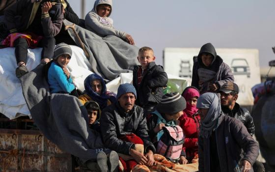 Adults and children, bundled up and carrying items, sit on back of vehicle.