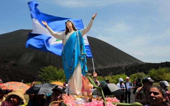 Statue of Mary as the Immaculate Conception carried by people, behind her waves Nicaraguan flag.