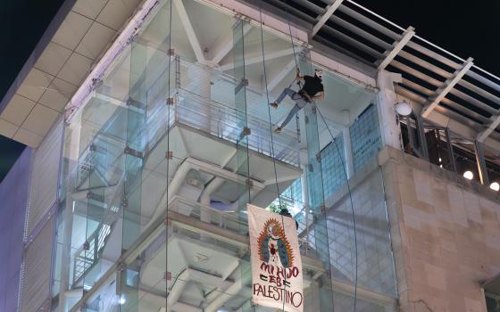 Person on rope against tall building, banner hangs.