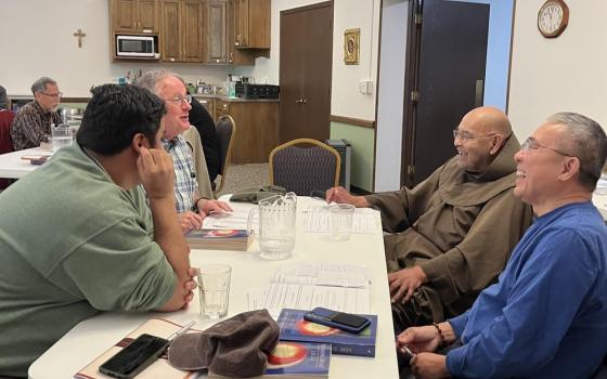 Four men sit around  table laughing and talking. 