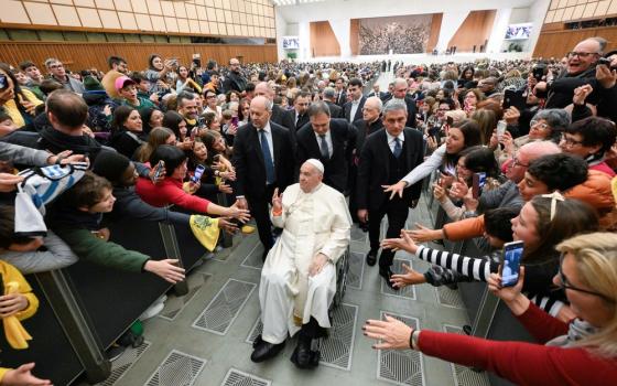 Francis in wheelchair surrounded by people waves and smiles.