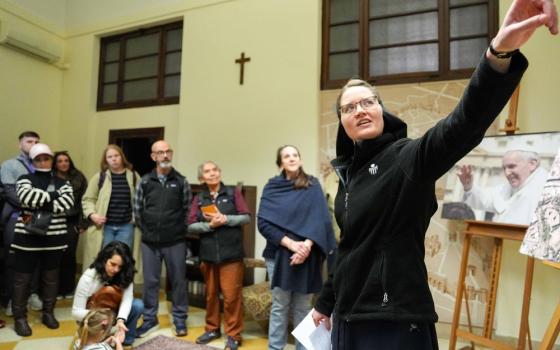 The sister foregrounded pointing out of frame, in background is small group assembled in classroom-like setting.