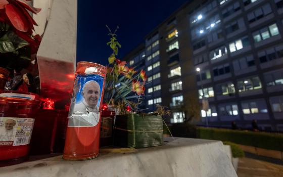 Votive candles, including some bearing a photo of Pope Francis, are seen on the base of a statue of St. John Paul II outside Rome's Gemelli hospital Feb. 15, 2025. (CNS photo/Pablo Esparza)