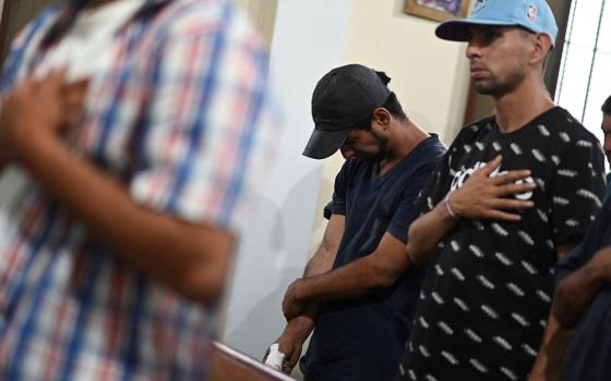 Two young men shown with heads bowed, one with hand over heart, standing in pews.