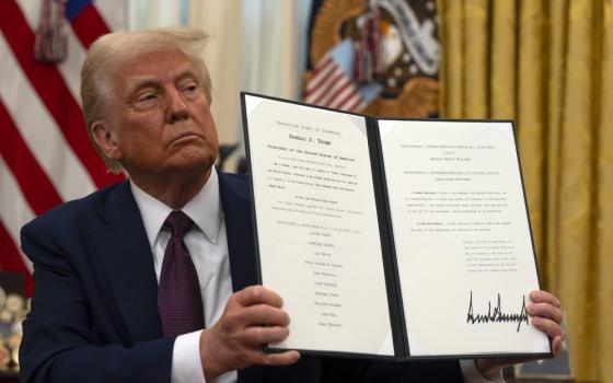 Trump sits holding up document. 