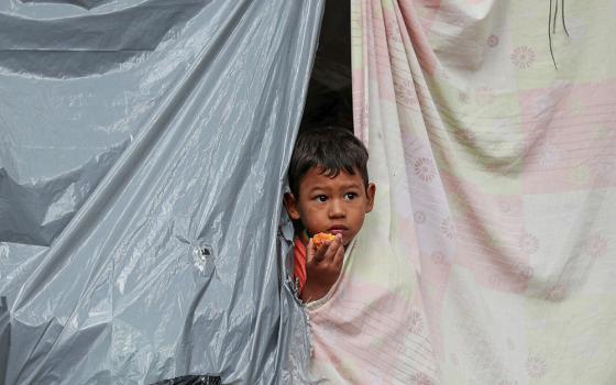 The child of a Venezuelan migrant peers from a tent at an encampment set up by migrants in a park near the main bus terminal in Bogotá, Colombia, June 3, 2020. Staff layoffs following the Trump administration's freeze on foreign aid in early 2025 have hit hardest so far in Colombia, where Jesuit Refugee Service assists Venezuelan refugees and others in accessing asylum to stay in that country. (AP Photo/Fernando Vergara)