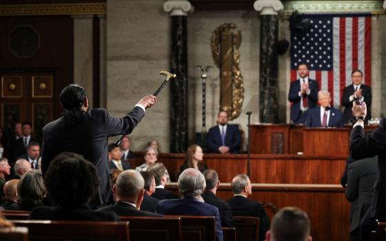 Green shown from behind shaking cane while Trump, seated, smiles smugly. 