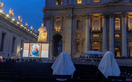 Nuns pray rosary in St. Peter's Square with large video scree.