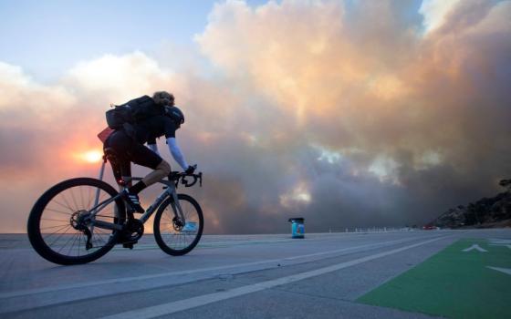 Man rides bike, with fire and windstorm in background