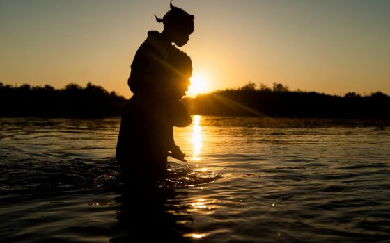 A migrant seeking asylum in the U.S. carries a child on his shoulder Sept. 20 as they cross the Rio Grande back into Mexico near the International Bridge between Mexico and the U.S. (CNS/Reuters/Go Nakamura)