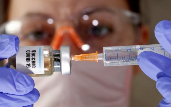 A woman holds a small bottle labeled with a "Vaccine COVID-19" sticker and a medical syringe in this photo illustration. (CNS Illustration/Reuters photo/Dado Ruvic)