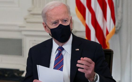 Joe Biden seated in black mask holding papers