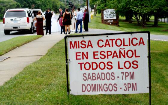 A sign announcing Masses in Spanish is seen as a wedding party gathers at Our Lady of the Assumption Church in Charlotte, North Carolina. (NCR photo/Peter Feuerherd)