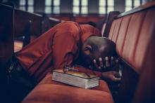 Man with head down on chairs, praying