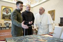 Francis, Zelenskyy, and a monk bend over a desk in the apostolic library to regard Zelenskyy's gift of an oil painting.