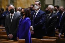 Harris, in blue suit and black face mask, stands in pew with hands crossed.