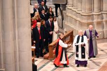 Bishop Budde wearing choir dress and holding large crozier processes past Trump.